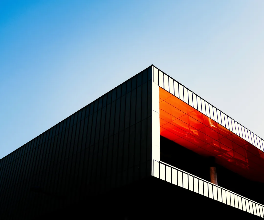 Angle d'un bâtiment à bardage sombre, sous-face orange, sur ciel bleu